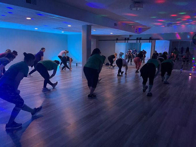 People stretching in a dimly lit dance studio with blue and purple lights.