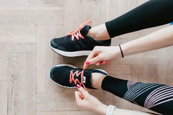 Hands tying black running shoes with pink laces on a wooden floor