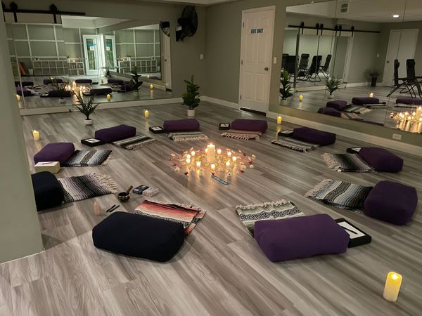 Candlelit yoga room with purple cushions and mats arranged in a circle on the floor