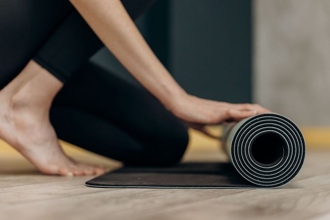 Person rolling out a black yoga mat on a wooden floor indoors