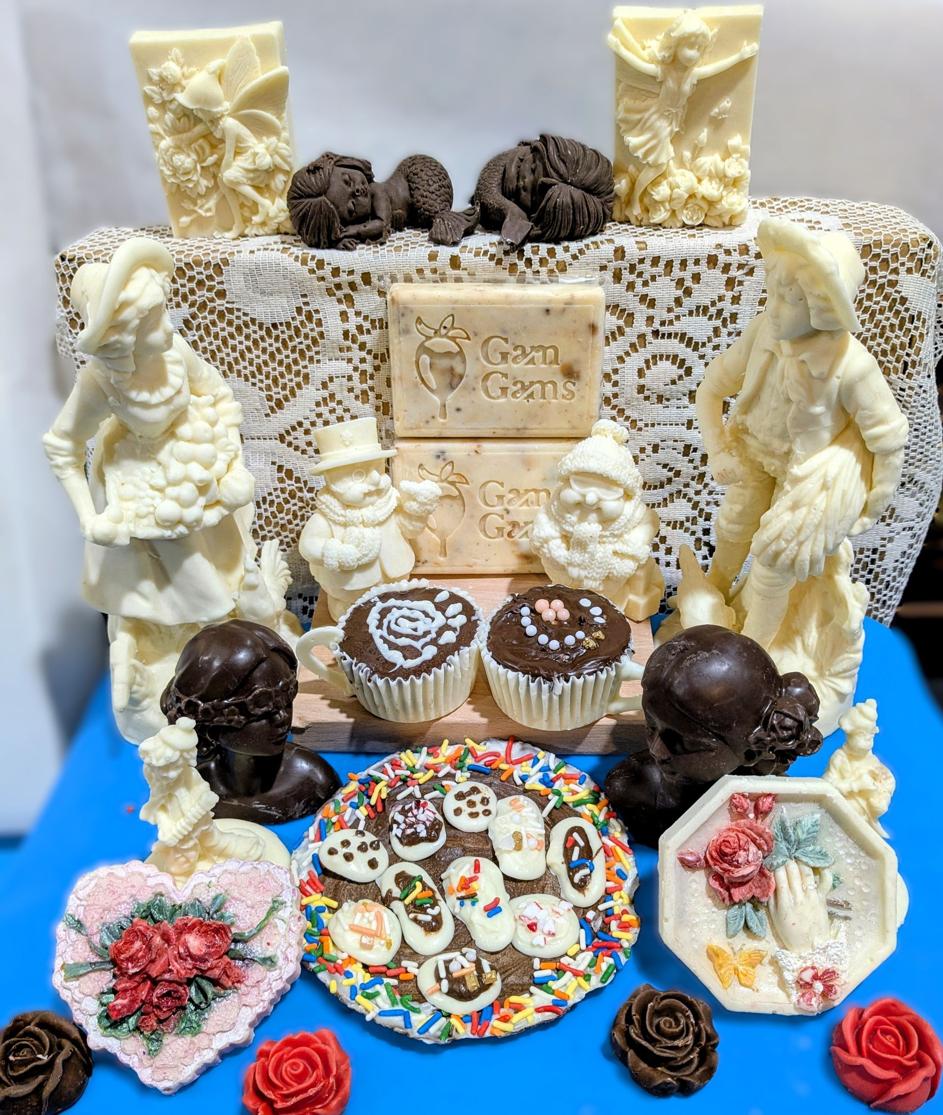 GamGams Chocolate Art. Decorated dessert display with chocolate treats, white icing, flowers, and colorful candies on a blue base.