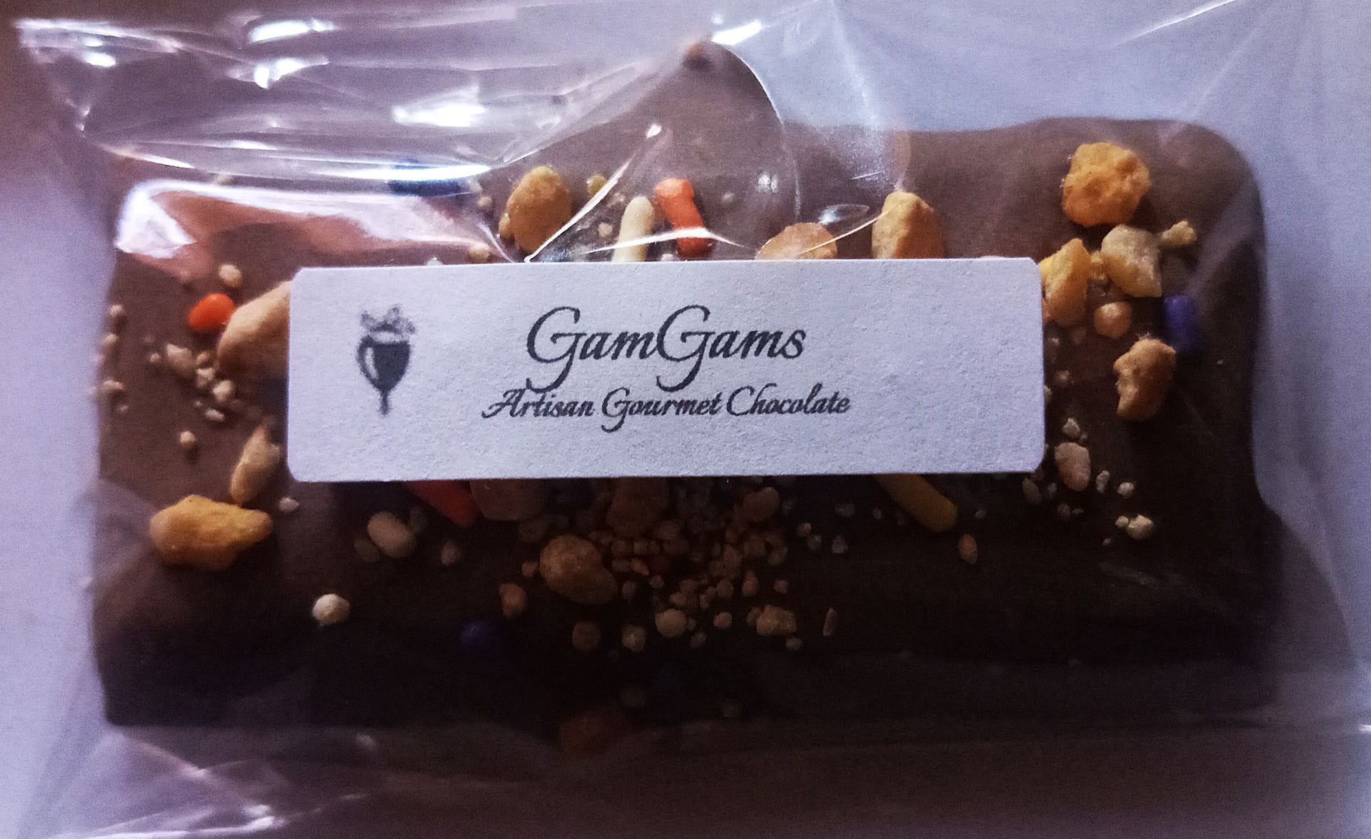 Chocolate cake in clear plastic packaging with a white label and nut topping