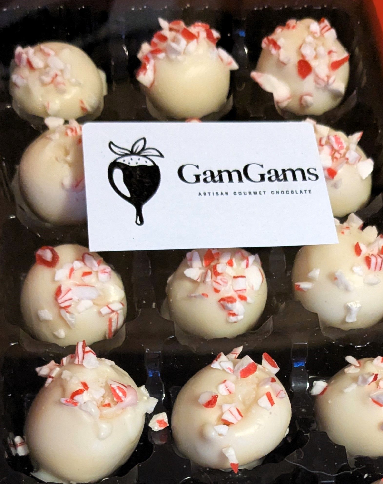 White candy truffles topped with red peppermint pieces in a black box with a GamGams card on top