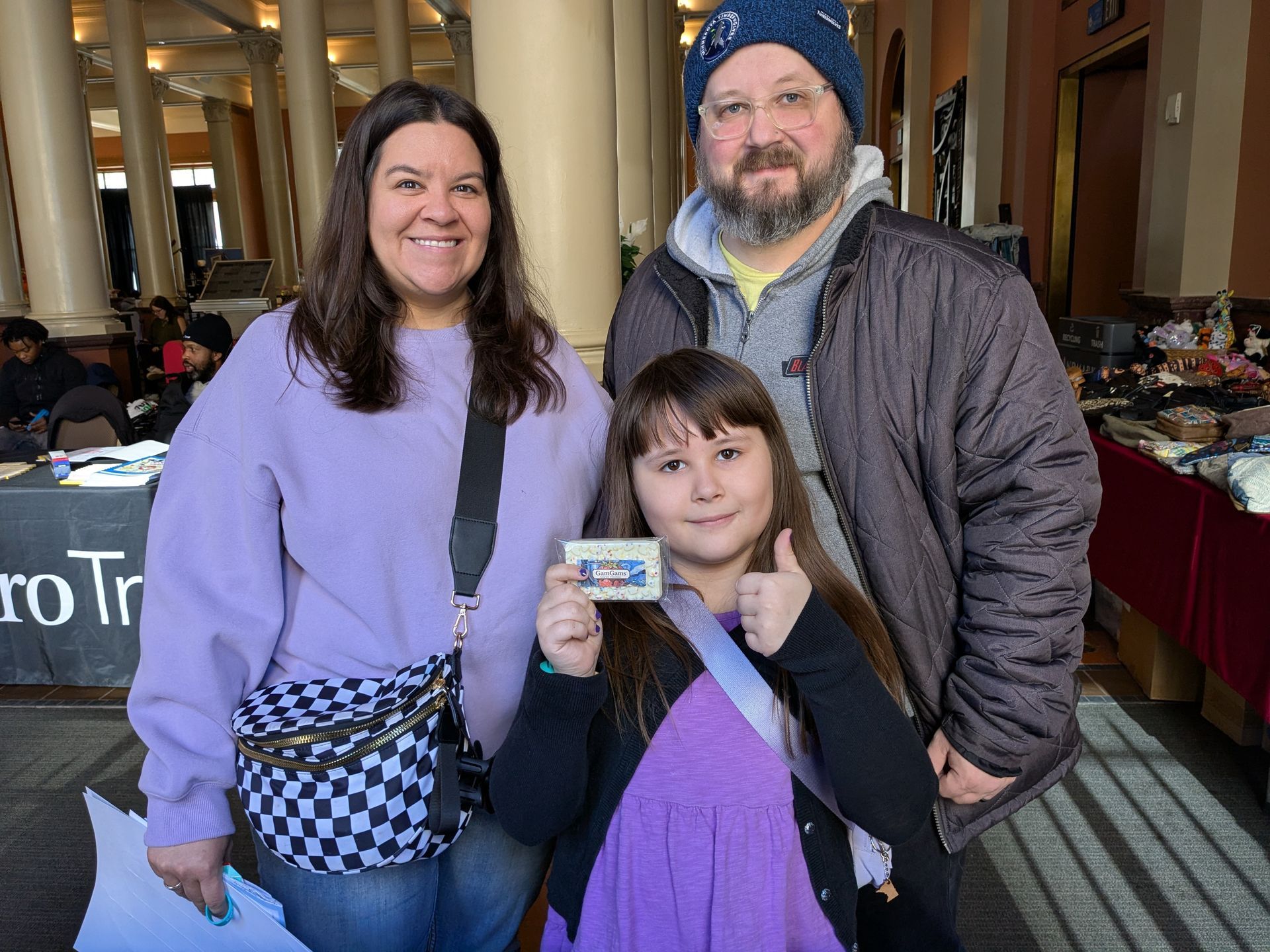 Three people posing indoors; a child holds up GamGams Chocolate Bar.