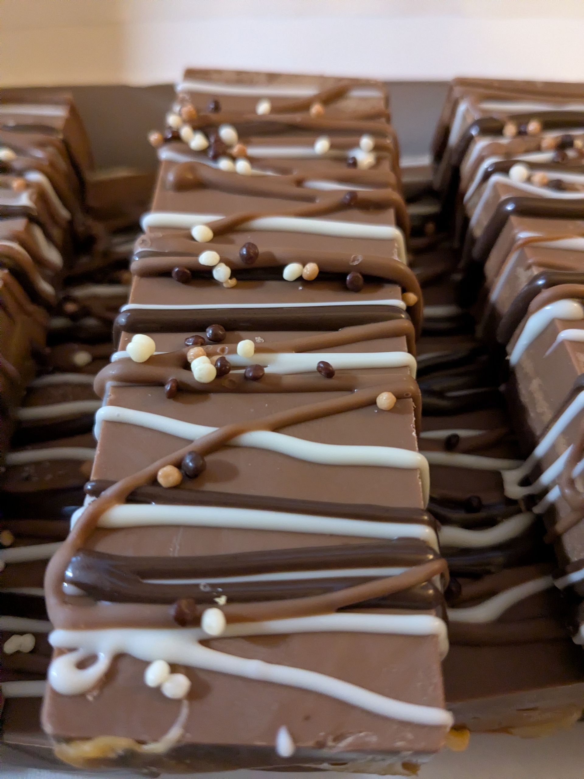 Rows of chocolate-covered dessert bars with white drizzle and sprinkles on a tray