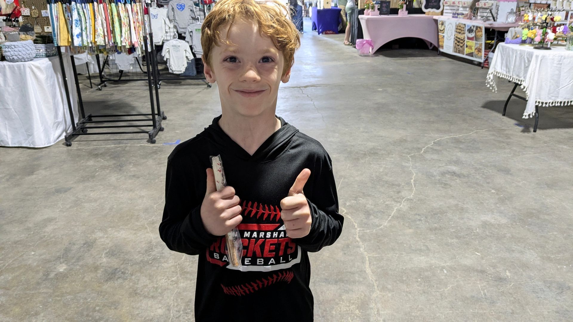 Child holding up a GamGams Pretzel Rod in a convention hall, standing at vendor tables.
