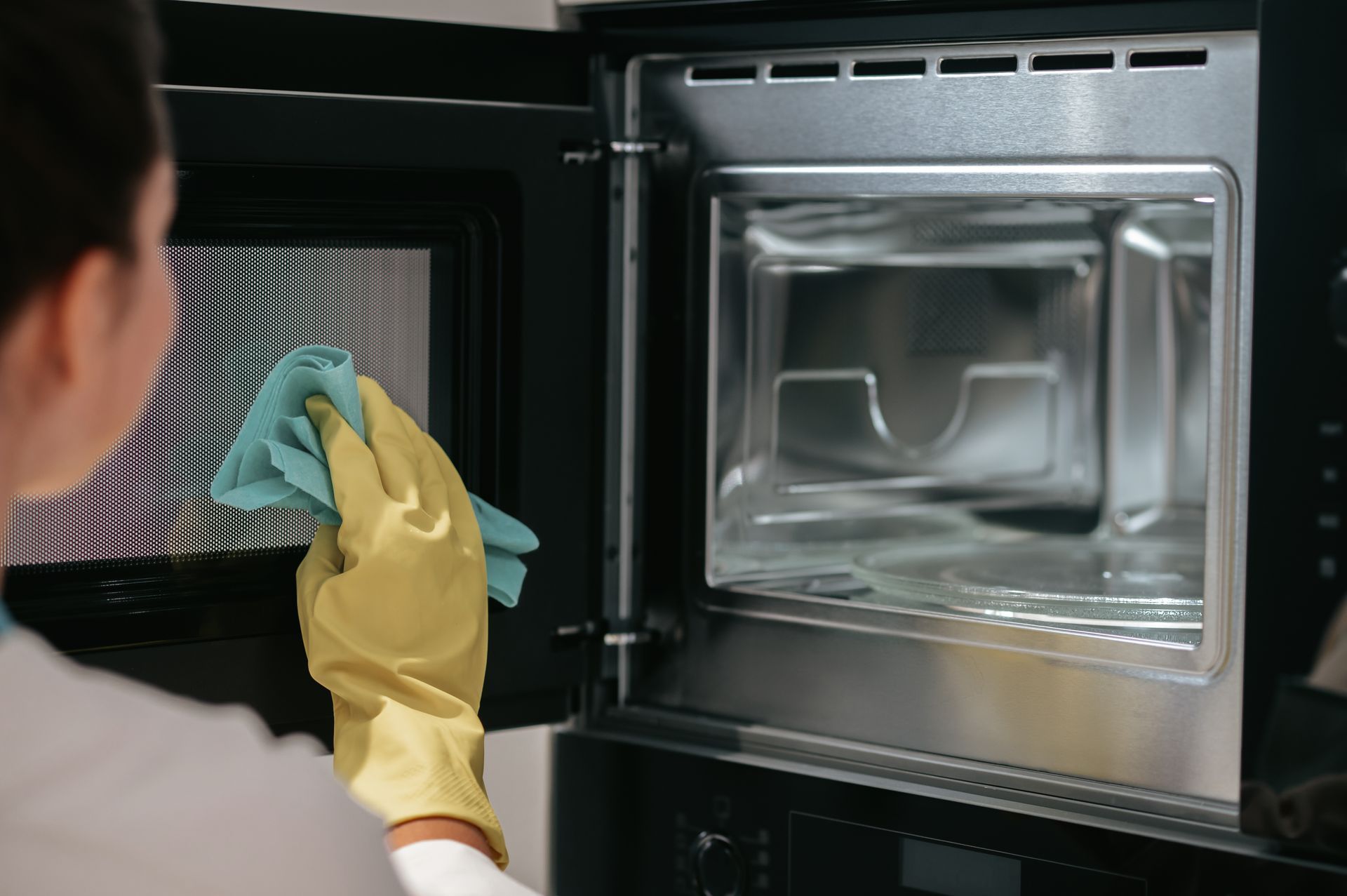A woman in yellow gloves is cleaning a microwave with a cloth.