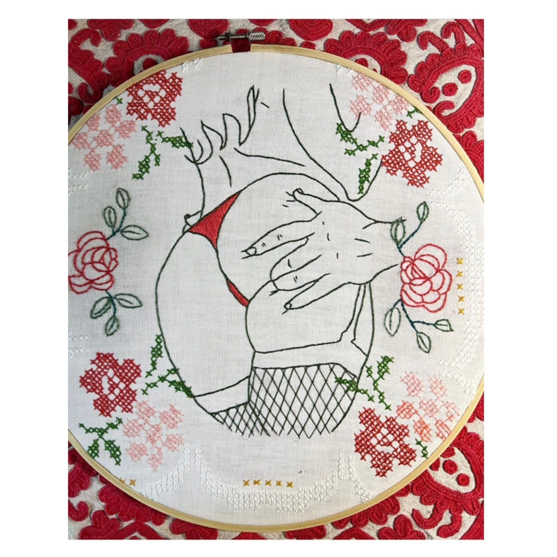 Embroidery hoop with a line drawing of a person's torso. Floral accents with red and pink cross-stitch.