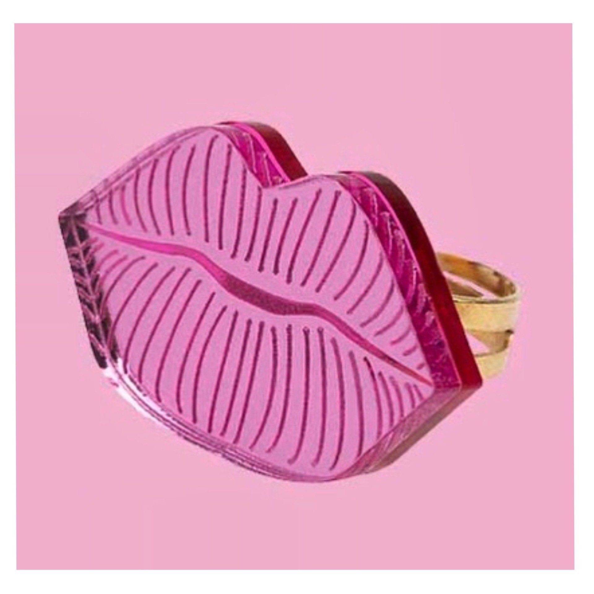 Pink lip-shaped ring with a gold band against a pink background.