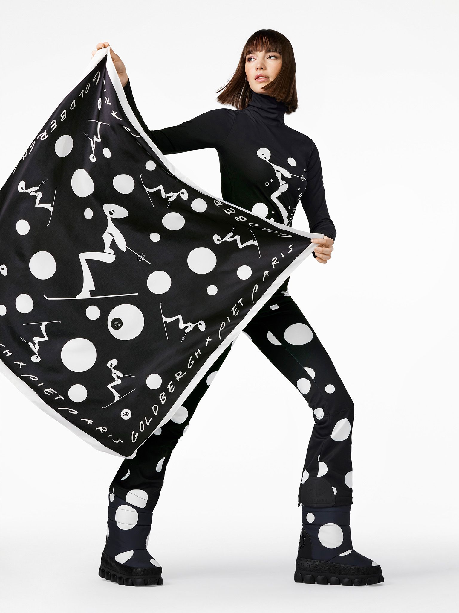 Woman in black outfit with white polka dots, holding a matching patterned scarf.