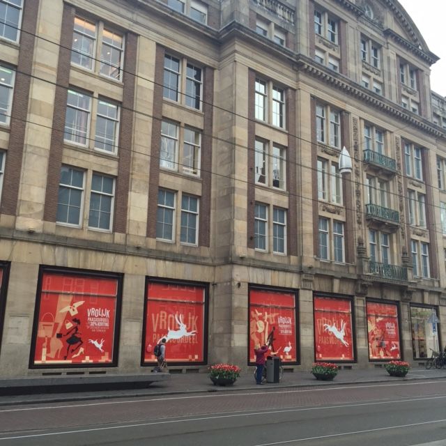 Building facade with red shop window displays, street with pedestrians, Amsterdam.