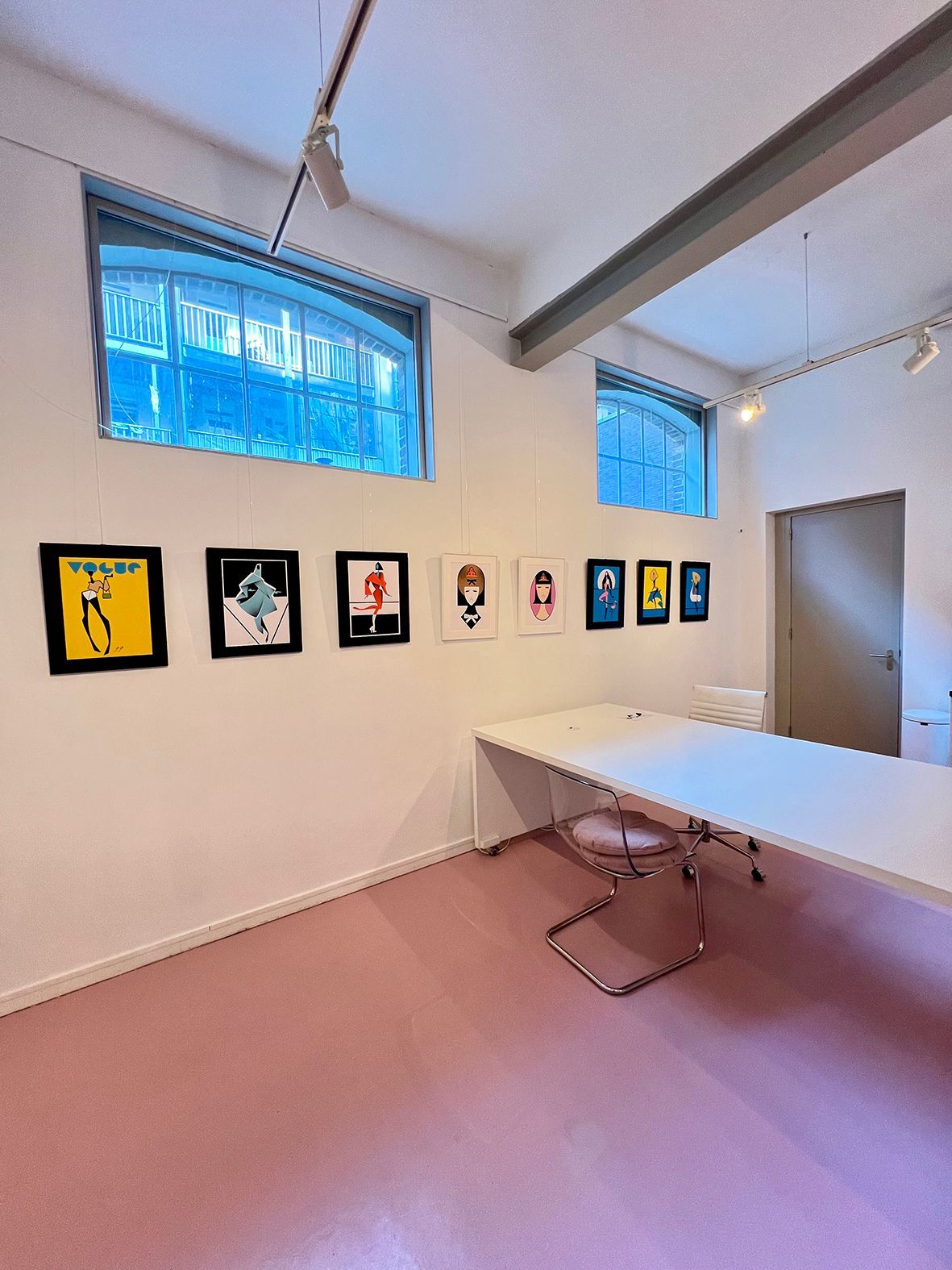 Art gallery interior with colorful framed artwork on a white wall, pink carpet, and blue glass block windows.Rental Space Venue at De Hallen Amsterdam
