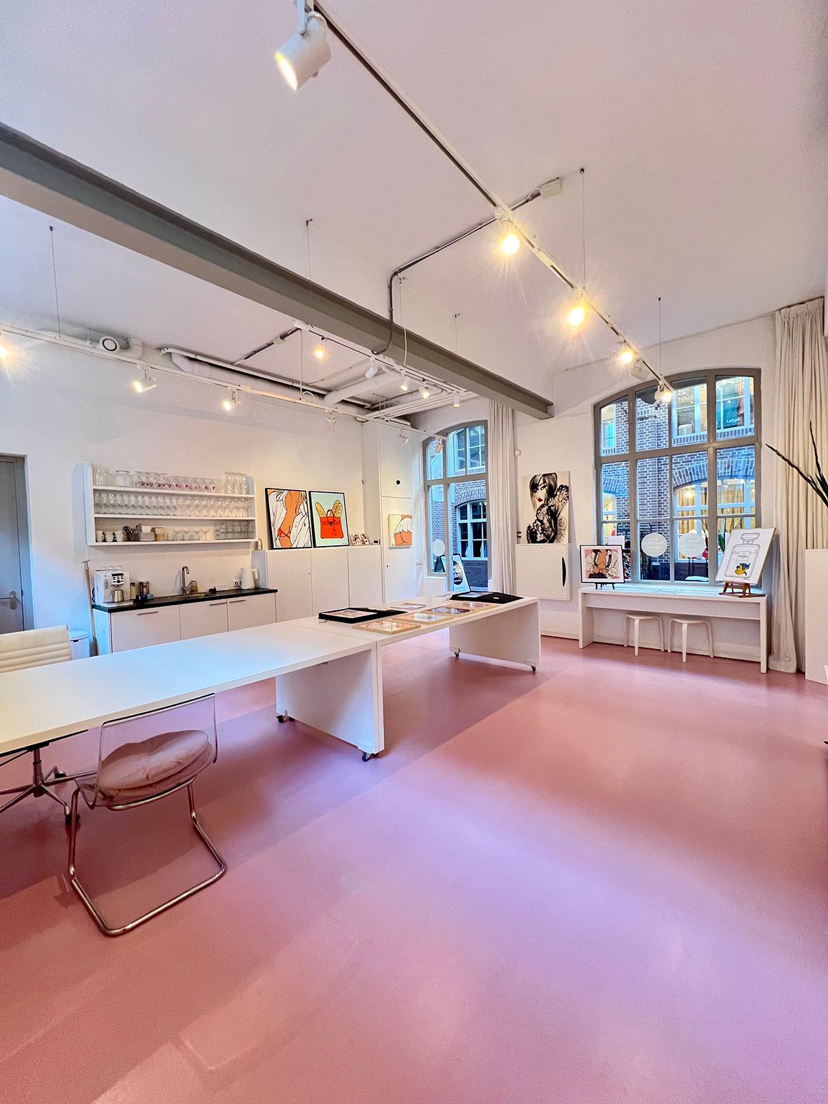 Pink-floored studio with long tables, artwork, and windows. White walls, exposed beams, and track lighting.Rental Space Venue at De Hallen Amsterdam