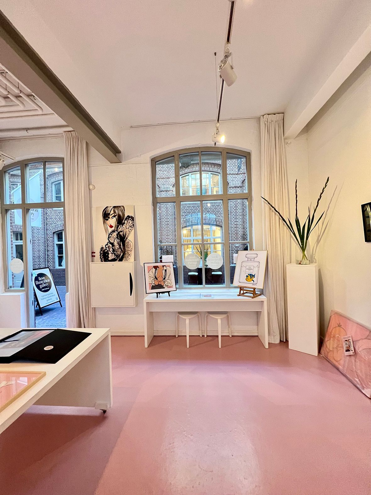 An art gallery interior with pink floor, white walls, large windows, and displayed artwork.Rental Space Venue at De Hallen Amsterdam