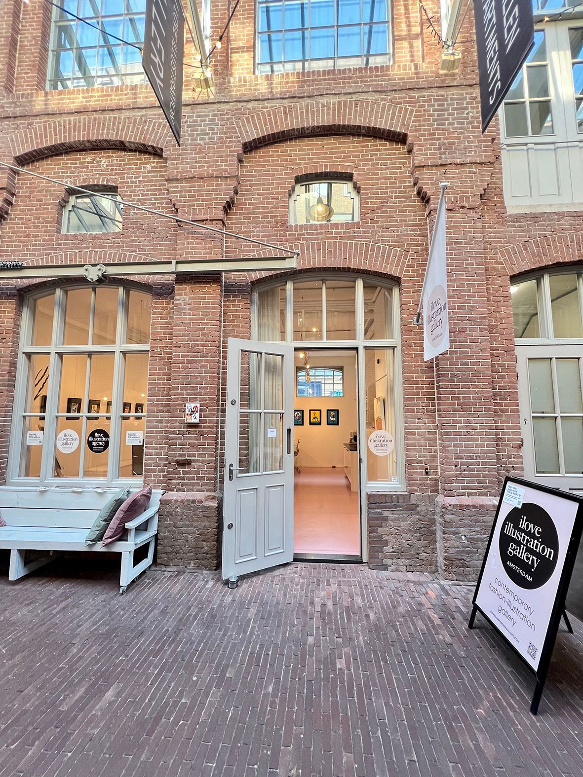 Exterior of a brick building with open doors, windows, and an A-frame sign; a bench is to the left.Rental Space Venue at De Hallen Amsterdam