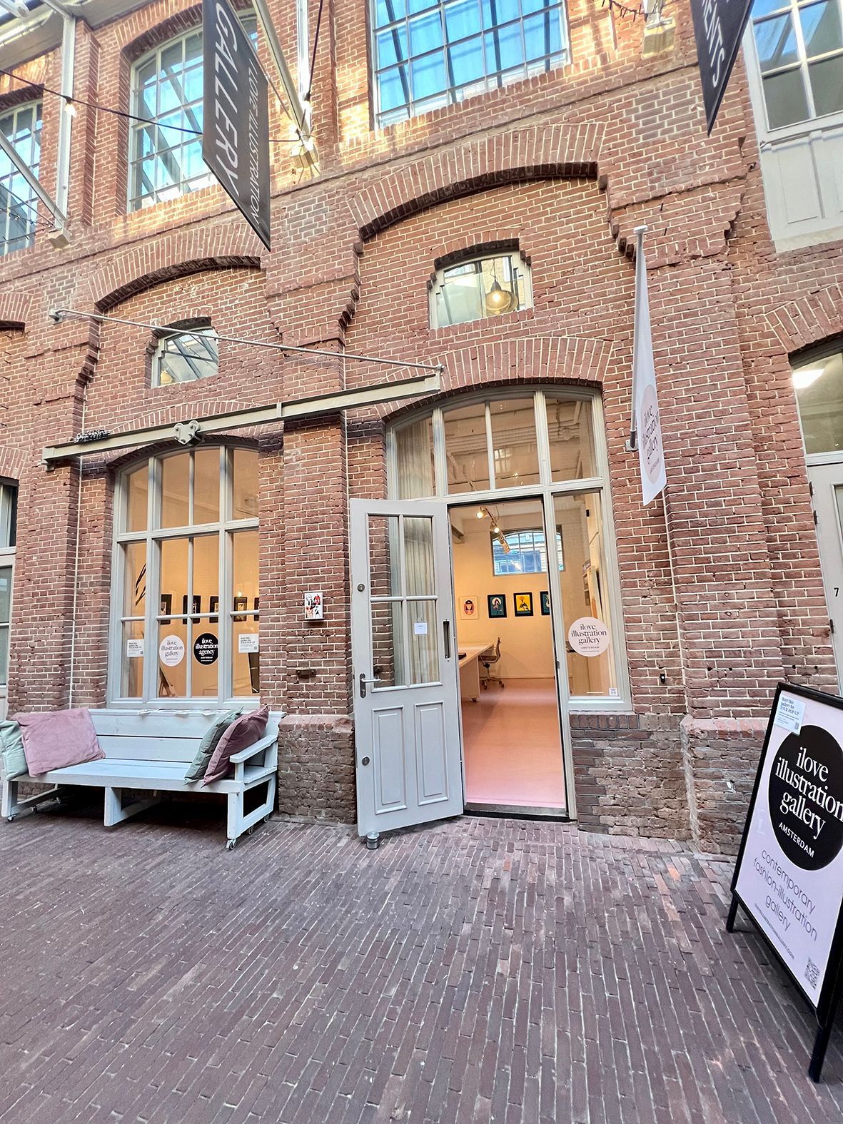Entrance to an art gallery with open door, brick building, bench, and sign.Rental Space Venue at De Hallen Amsterdam