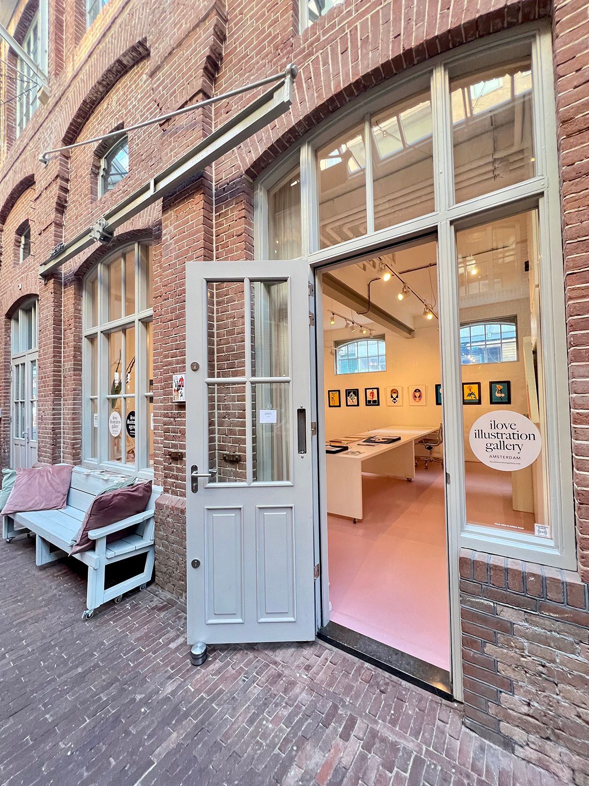 Exterior of an art gallery with open door. Pink interior, brick building, bench. Rental Space Venue at De Hallen Amsterdam