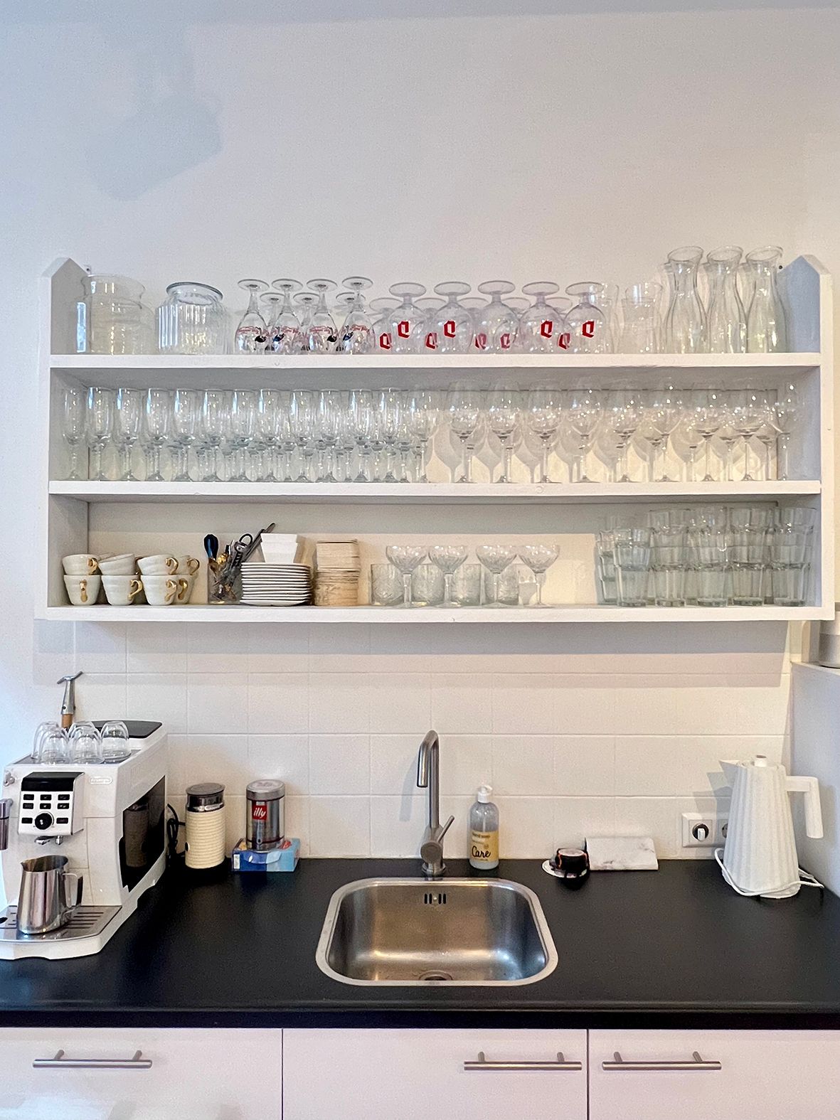 White kitchen shelving displaying glassware above a sink on a black countertop.Rental Space Venue at De Hallen Amsterdam