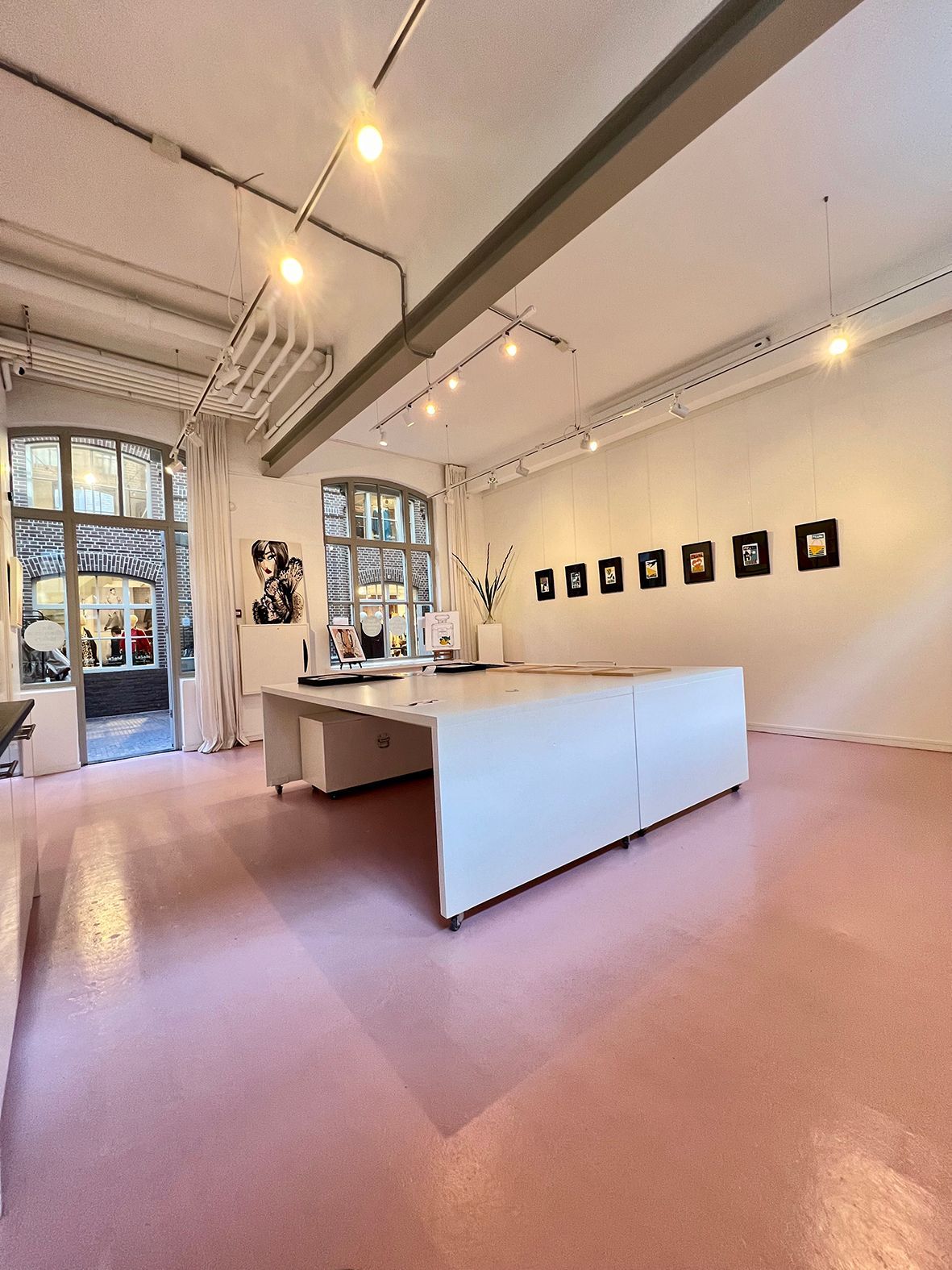 Empty art gallery with pink floor, white walls, large white table, and artwork displayed. Rental Space Venue at De Hallen Amsterdam