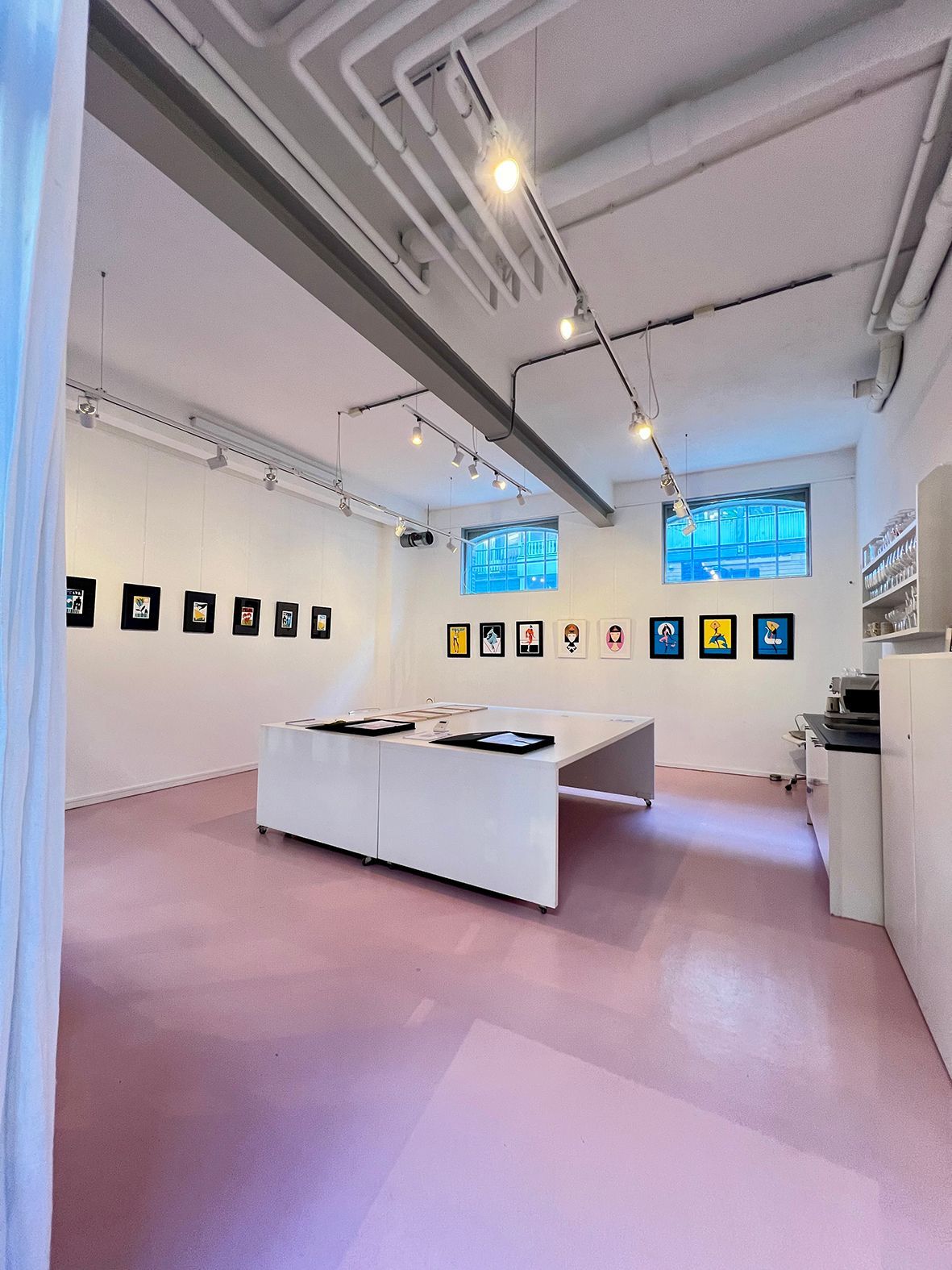 Art gallery interior with pink floor, white walls, artwork displayed, and a large table. Rental Space Venue at De Hallen Amsterdam