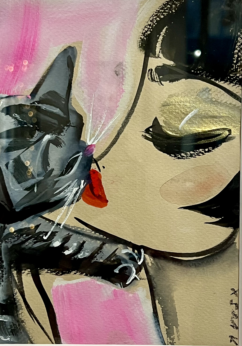 Cat nuzzles a woman's face. The cat is gray and black with a red bow tie. The woman has closed eyes with gold eyeshadow.