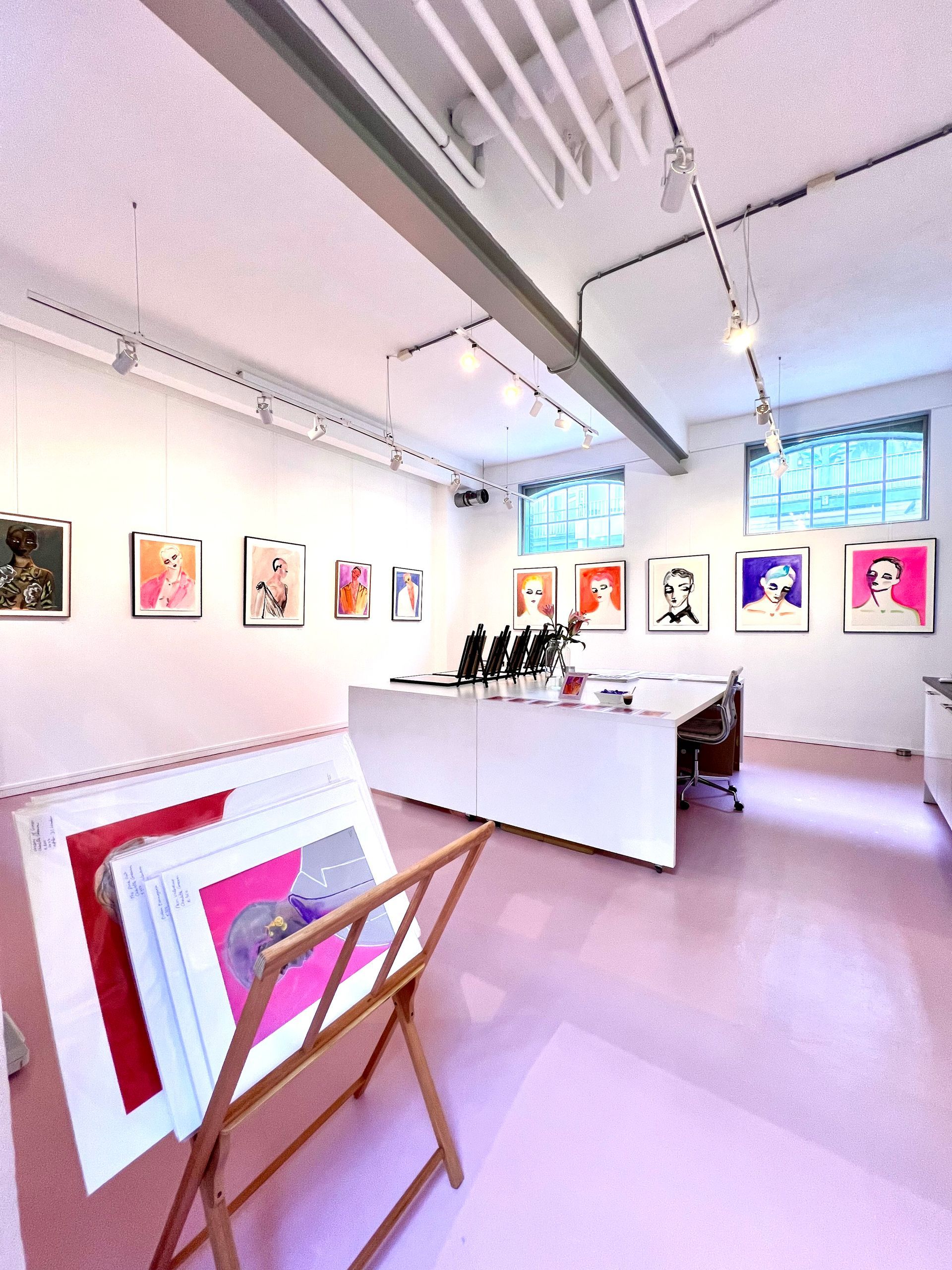 Art gallery interior, pink floor, white walls, framed art on display, work table, and prints on an easel.Rental Space Venue at De Hallen Amsterdam