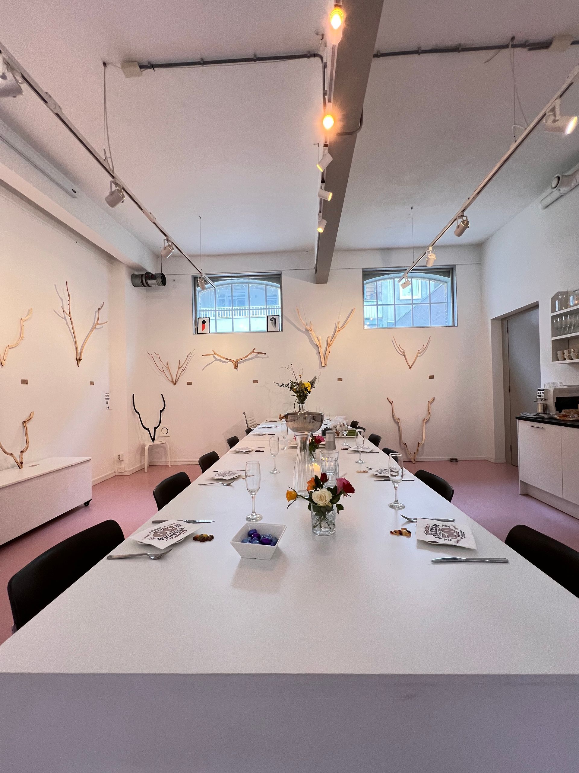 Long white table set for a meal in a bright room with pink floor.Rental Space Venue at De Hallen Amsterdam