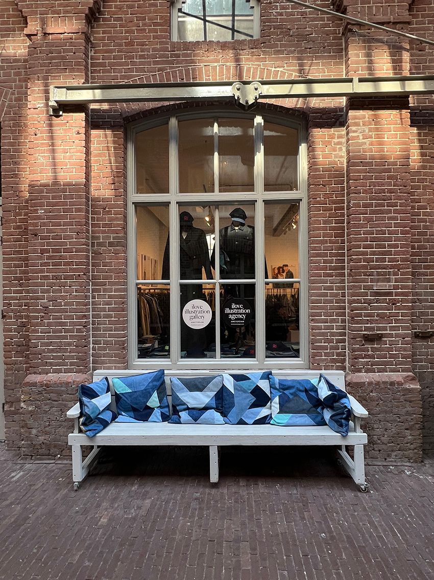 Brick building with large window displaying mannequins, and a white bench with denim pillows and blanket. Rental Space Venue at De Hallen Amsterdam
