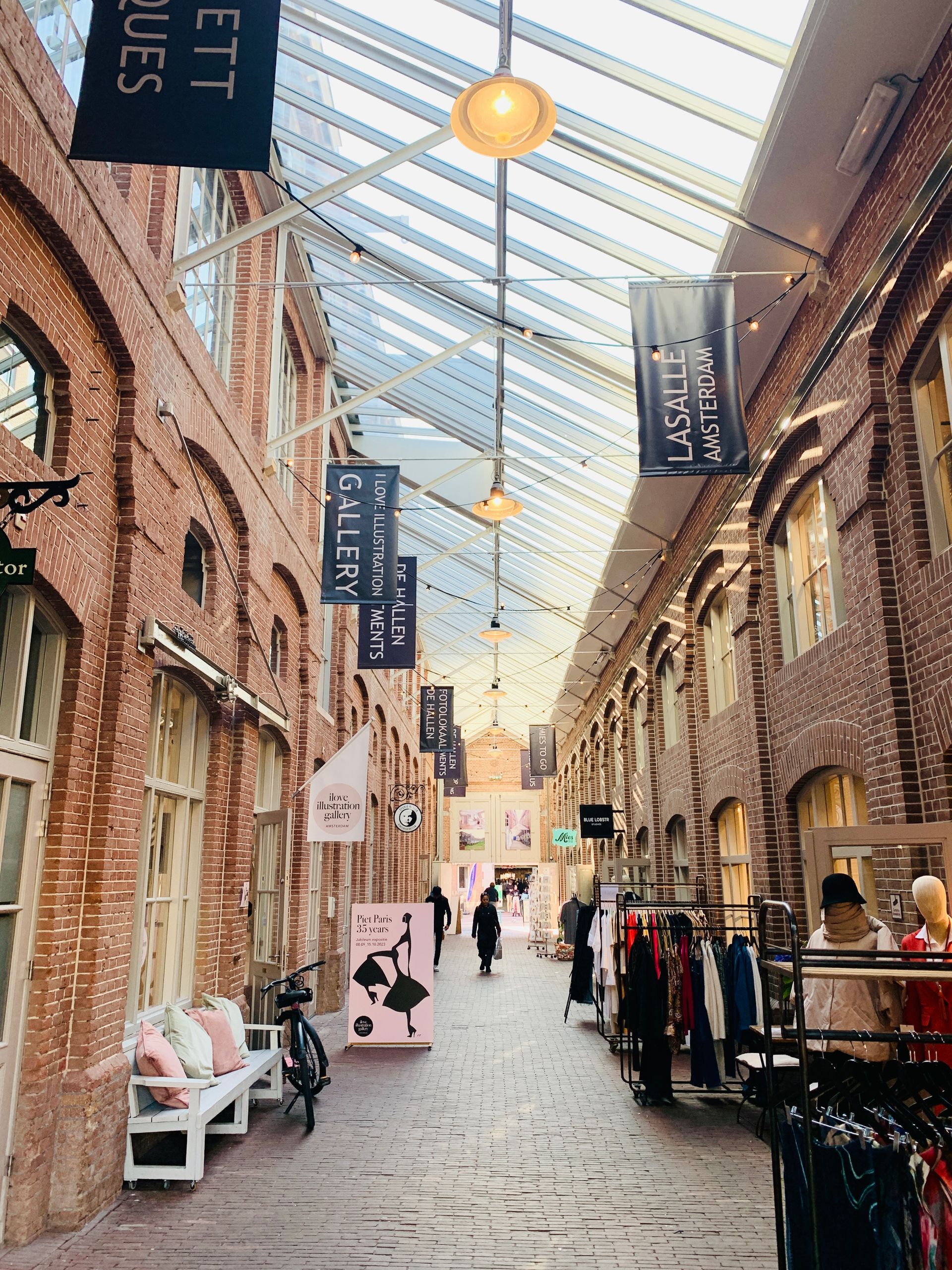 Indoor shopping mall with a brick facade, glass roof, and banners hanging.Rental Space Venue at De Hallen Amsterdam