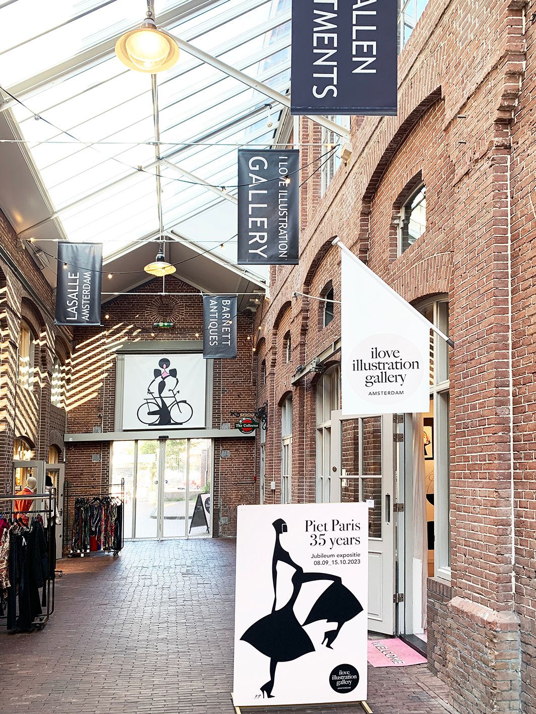 An interior mall walkway with brick walls and hanging shop signs, including 