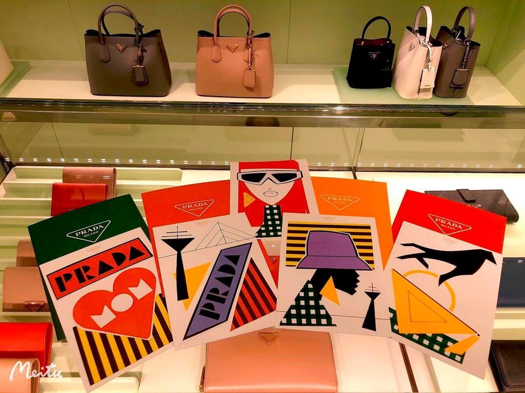 Prada store display: handbags on shelves above colorful Prada art prints and wallets.