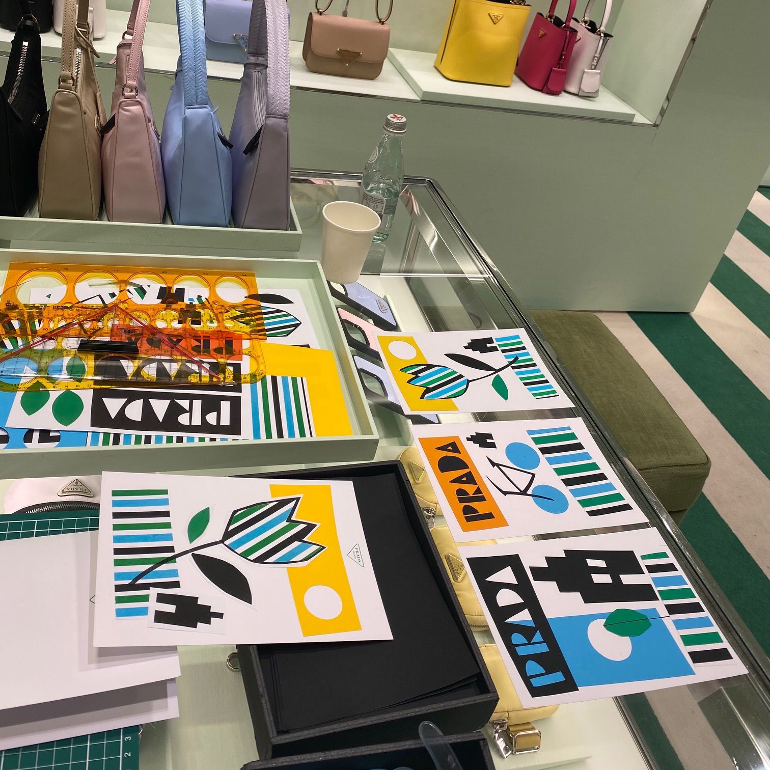 Display of Prada bags and art prints on a table; bags are in various colors.