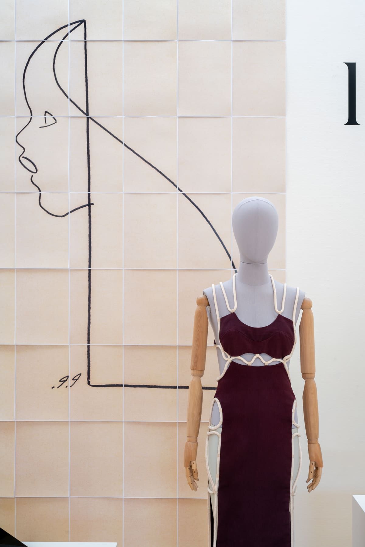 Mannequin in burgundy dress with a skeletal white outline, beside a face sketch on a grid background.
