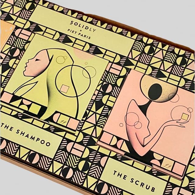 Boxes of shampoo and scrub with stylized art on them, geometric background.