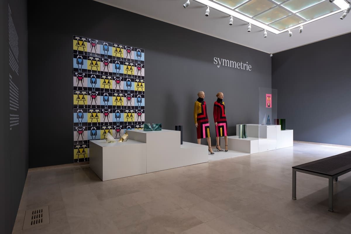 Fashion display in a modern gallery with mannequins, geometric backdrop, and white platforms.