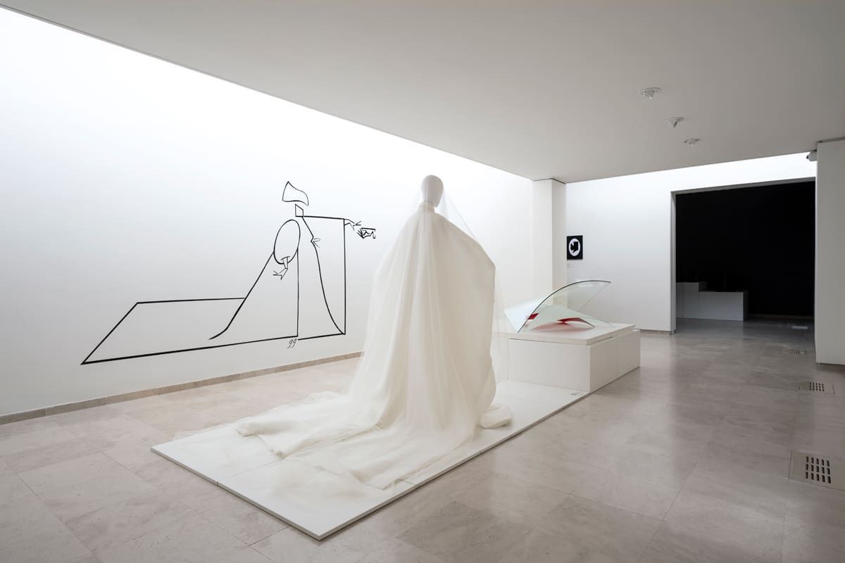 White art gallery with a draped figure, minimalist drawing on wall.