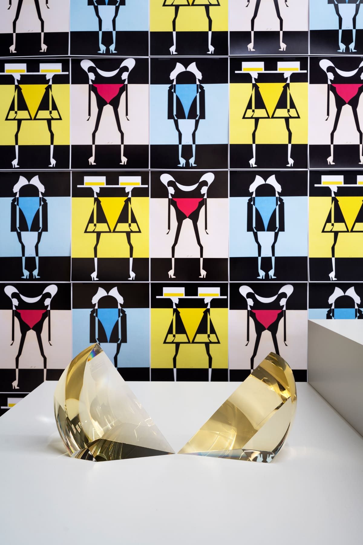 Abstract figures in primary colors on tiled wall. Two gold, abstract sculptures on white surface.