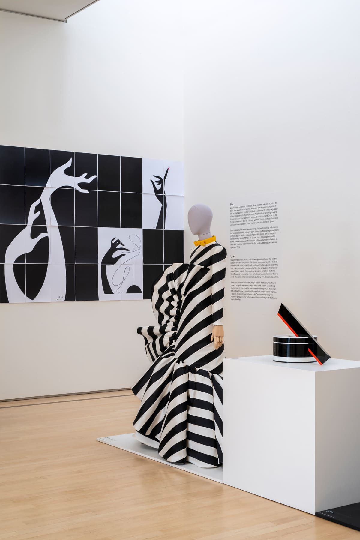 Mannequin in black and white striped dress next to graphic art in a museum.