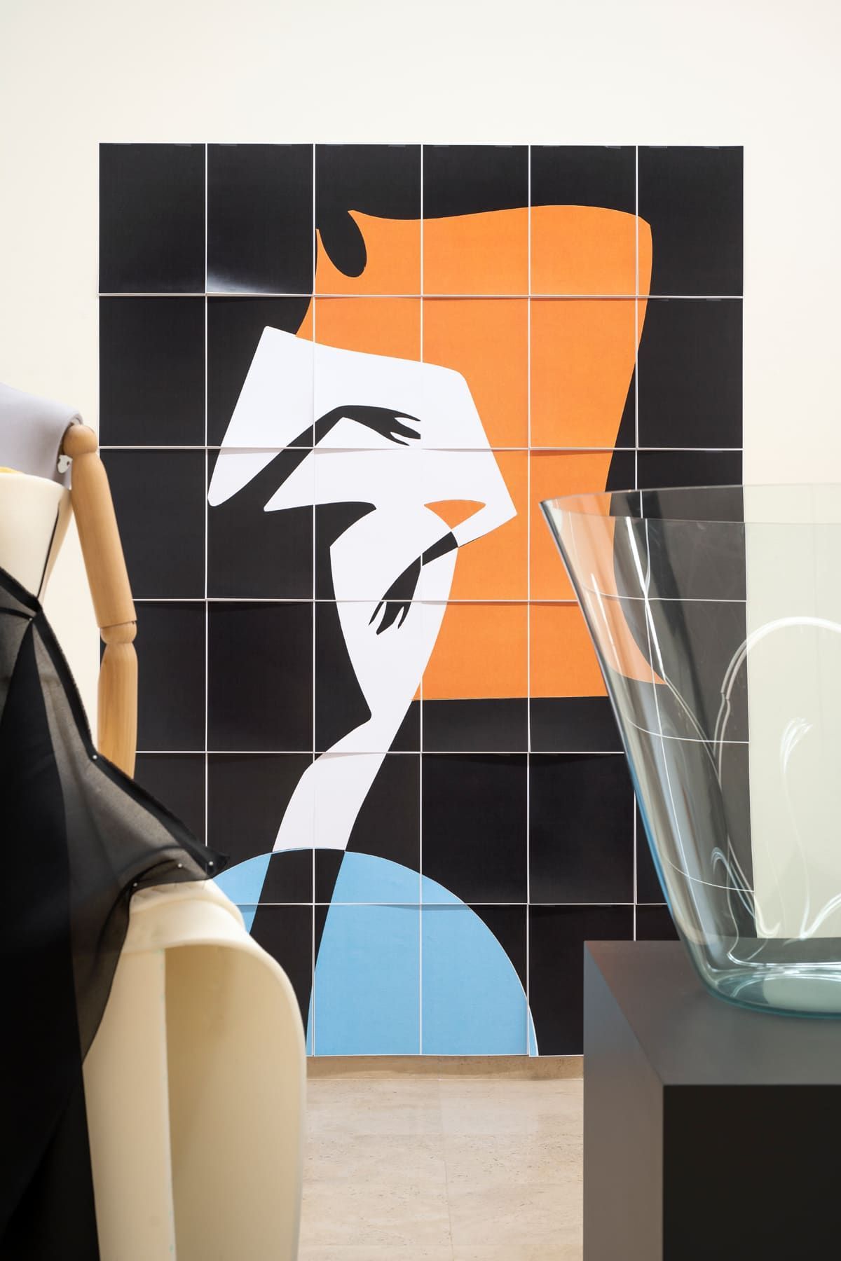 Abstract artwork: black and orange figure, geometric lines, blue arcs, beside a mannequin and glass vase.