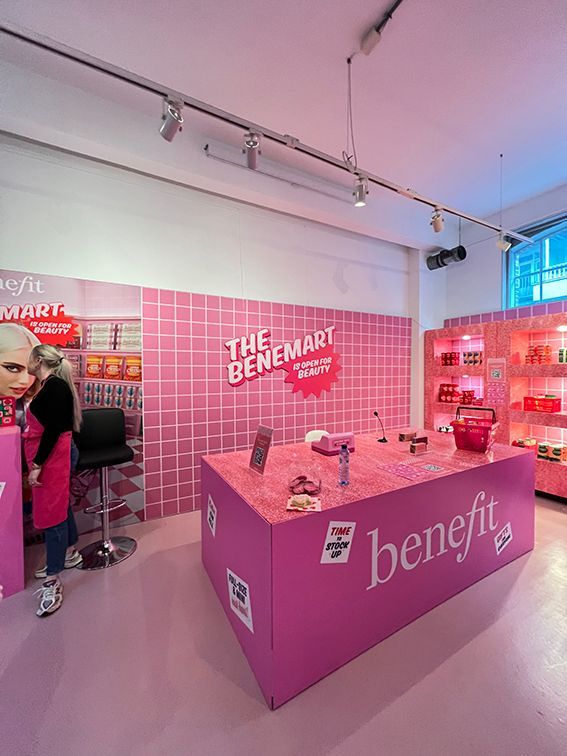 Pink Benefit cosmetics store: display table with products, pink walls, customer, and 