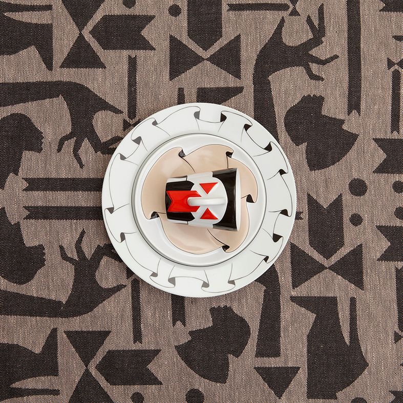 Dishes on patterned tablecloth; cup with red and black design in center.