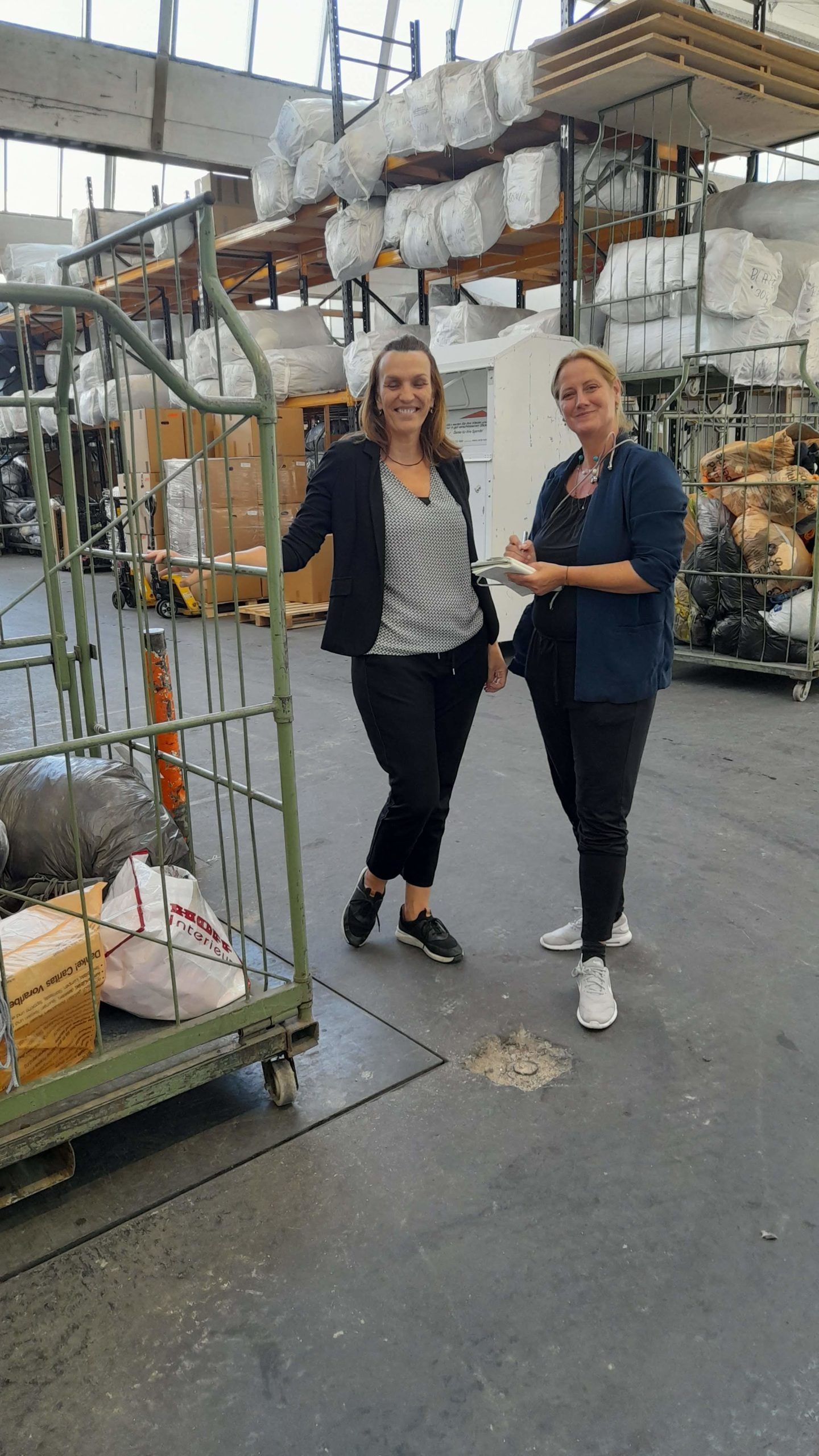 Zwei Frauen stehen nebeneinander in einer Lagerhalle.