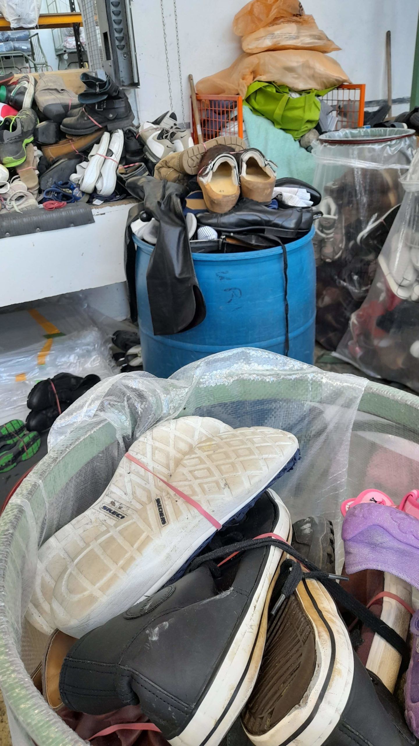 Auf einem blauen Fass liegt ein Stapel Schuhe.