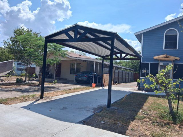 Covered carport beside a driveway and house under a sunny blue sky