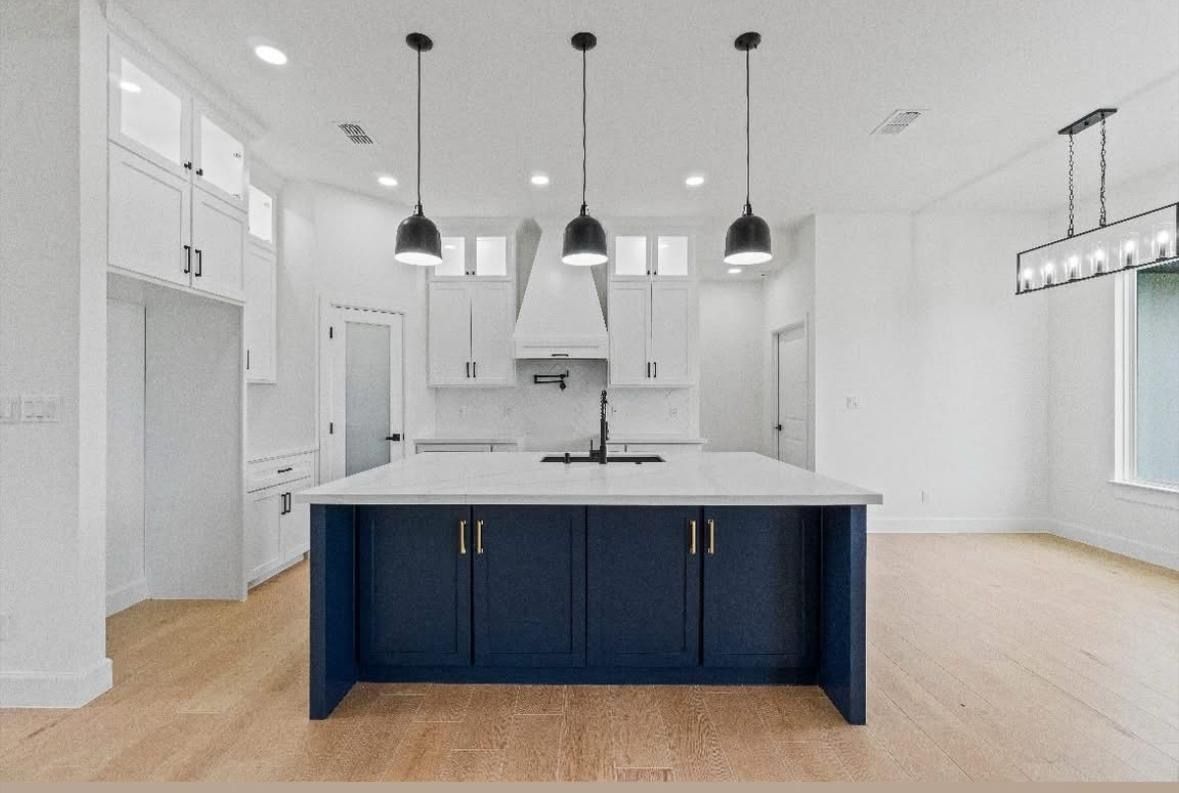 Bright modern kitchen with navy island, white cabinets, pendant lights, and light wood floors