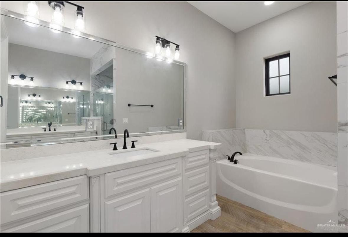 Bright white bathroom with double vanity, large mirrors, and a freestanding tub by a window.