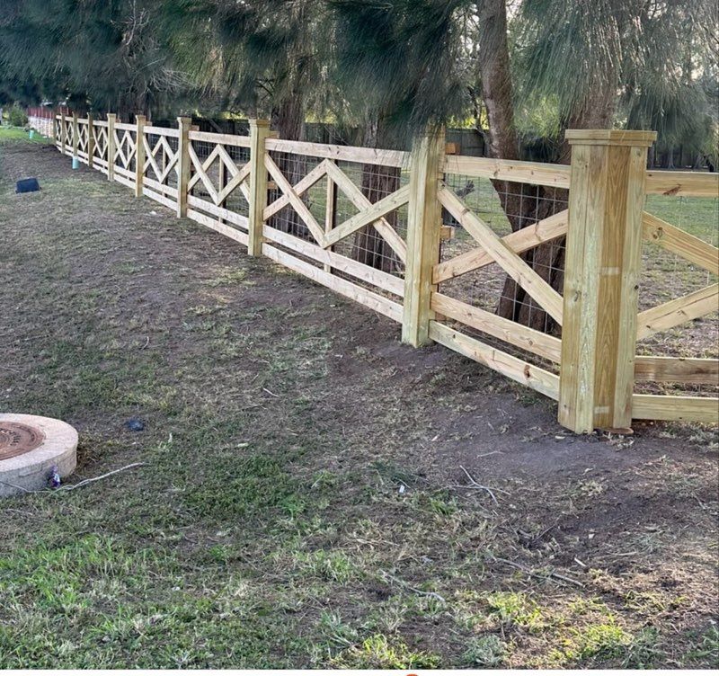 Wooden fence with crisscross rails along a dirt and grass yard with trees in the background