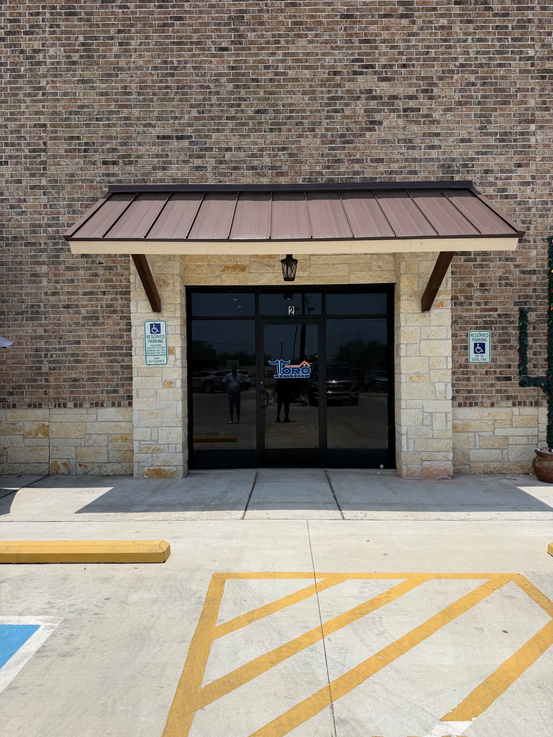 Brick storefront entrance with dark glass double doors, small awning, and accessible parking markings in front