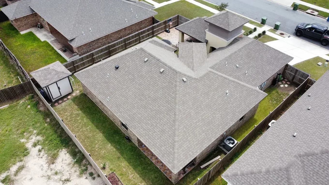 Aerial view of a gray-roofed suburban house with fenced yard and neighboring homes.