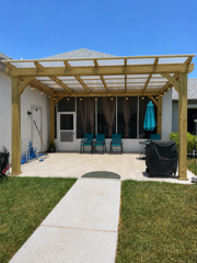Backyard patio with pergola, patio chairs, grill, and a walkway leading through the grass